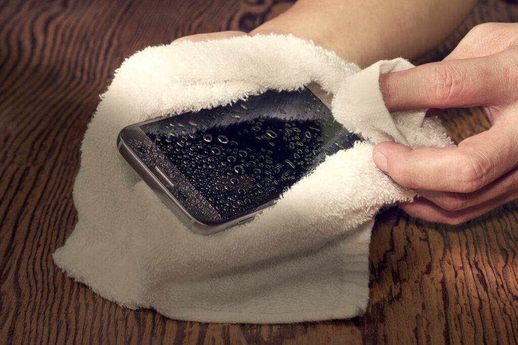 Closeup hands holding white cloth with wet smart phone drops wooden floor Closeup hands holding white cloth with wet smart phone drops wooden floor